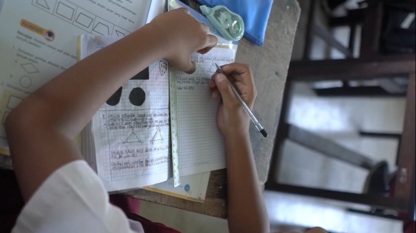 Tangan siswa sekolah dasar menulis dan menggambar bangun datar di buku tulis